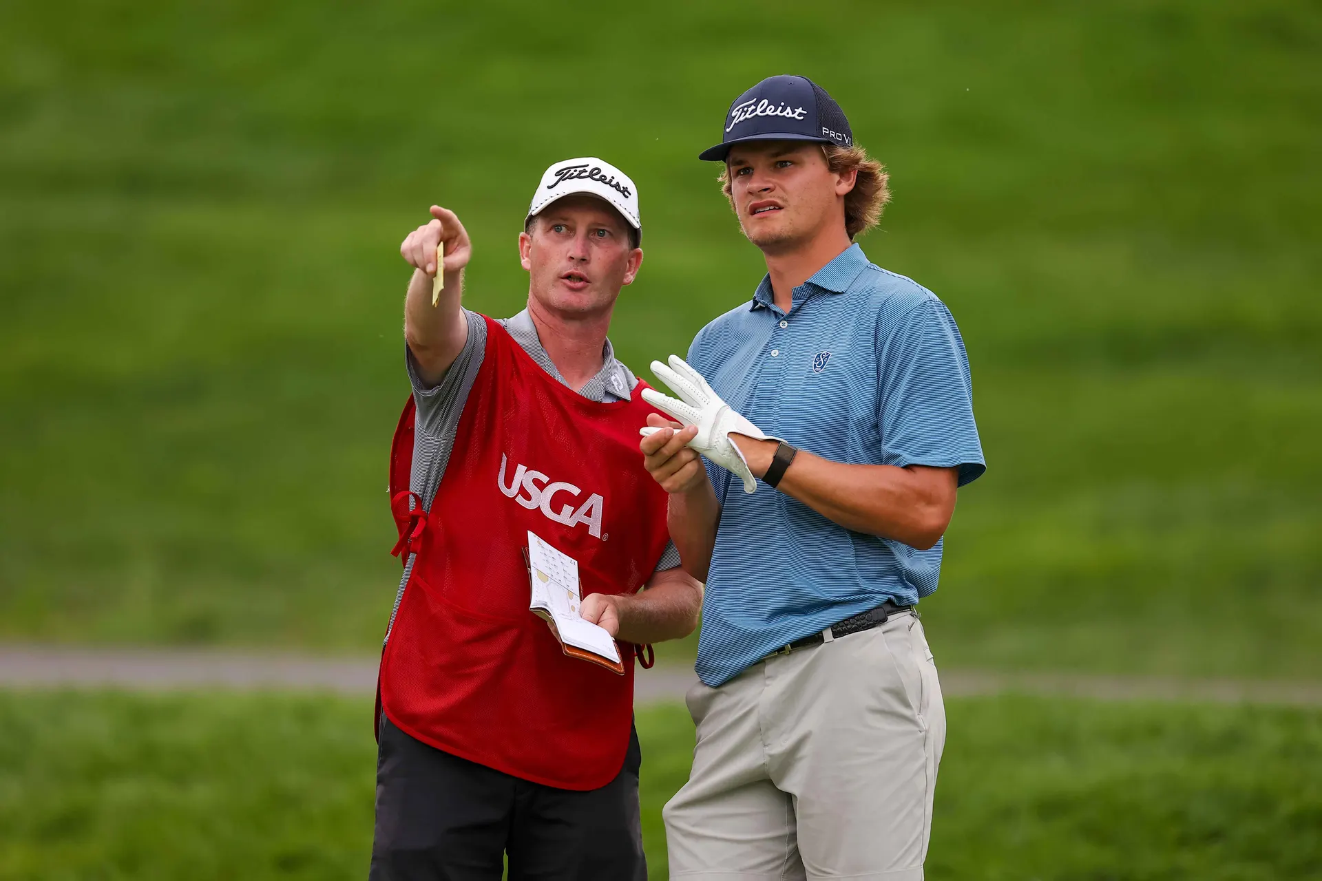 Ryan Sharpe caddying at a USGA championship, reading a yardage book and pointing out the line to his player